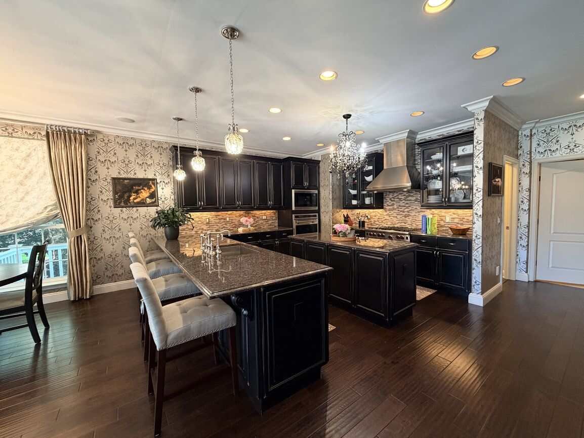 Open kitchen with dark custom cabinetry, granite island with seating, stainless Wolf range, and chandelier lighting