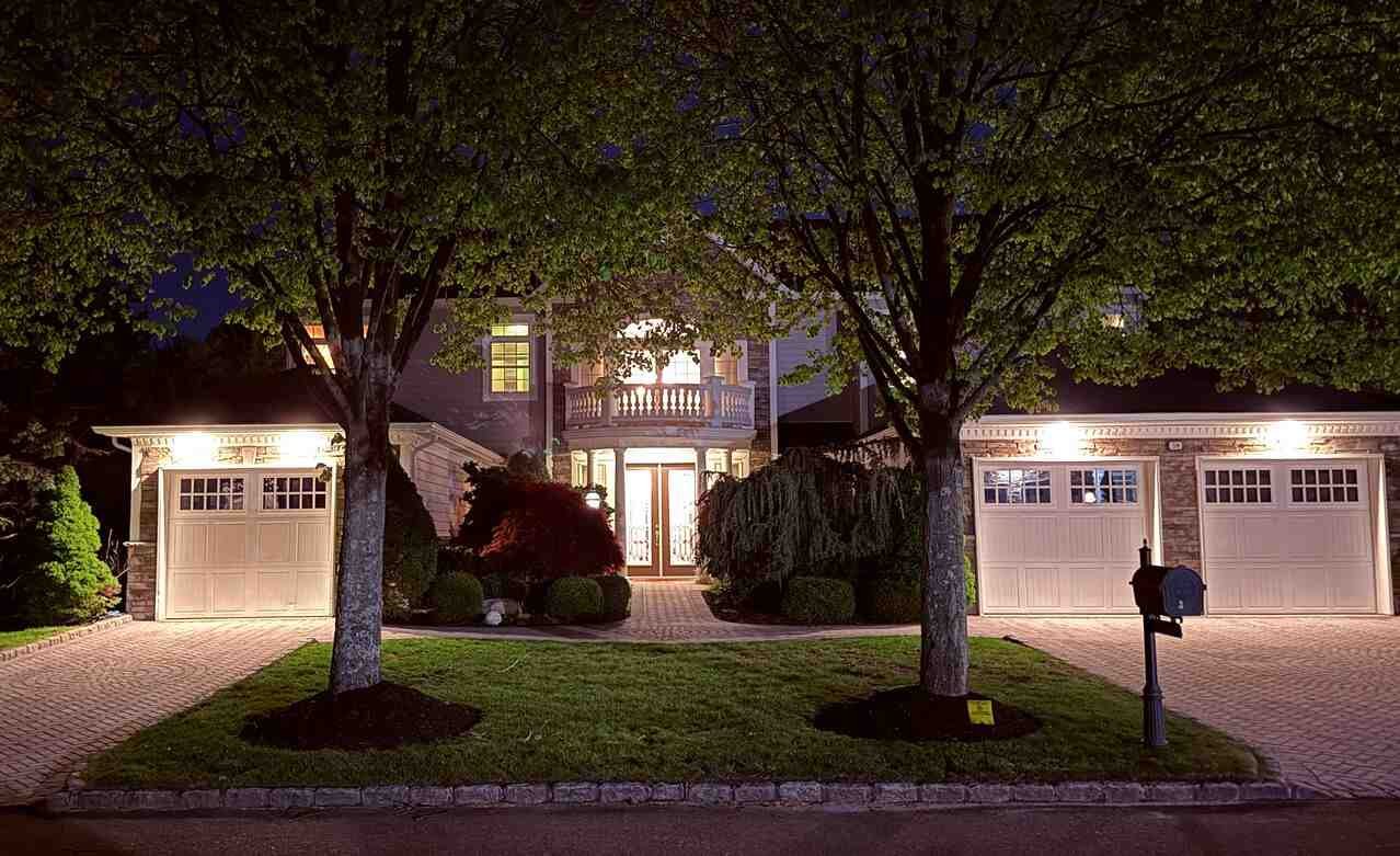 Front of 38 Hamlet Woods Drive at night with the entry, balcony, and three-car garage bays lit